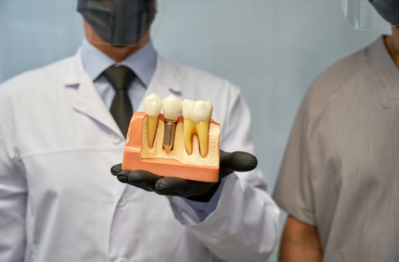 Dentist holding dental implant model showing titanium post, abutment, and crown in Austin TX